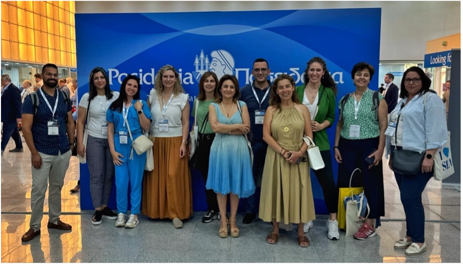 A group of people standing in front of a blue sign    Description automatically generated